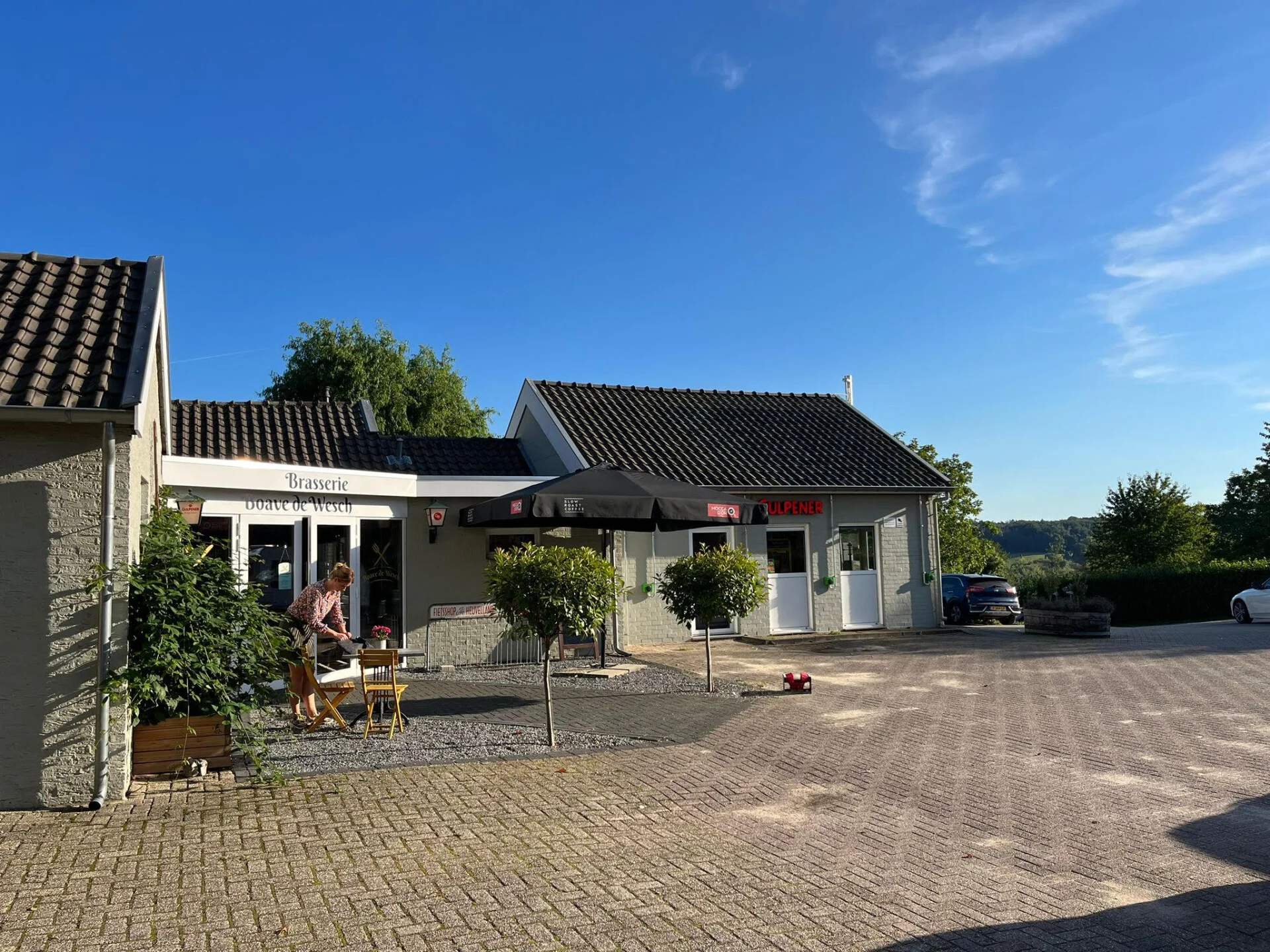 Vooraanzicht van Brasserie Boave de Wesch met terrasstoelen en parasol in de zon
