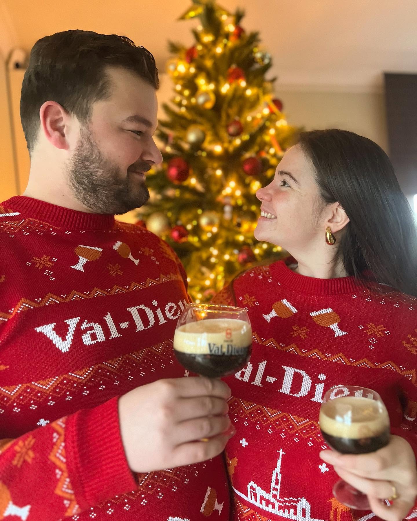 Marieke en Moreno kijken elkaar lachend aan en proosten met een glas bier voor een verlichte kerstboom